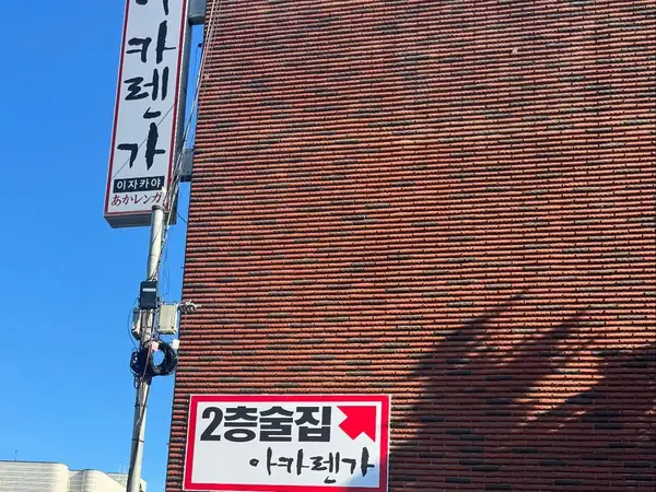 붉은 벽돌 건물 모서리의 흰 세로 간판과 ‘2층술집’ 안내판